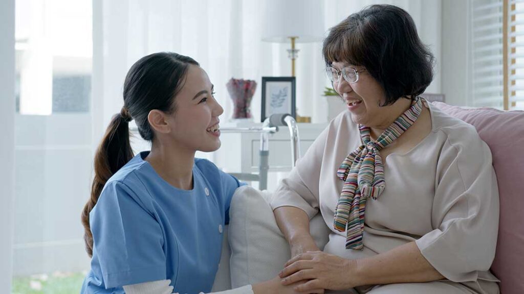 A senior resident using a tablet for video calling while sitting in a comfortable living room chair.