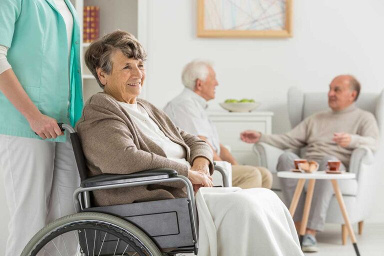 Three older adults painting flower pots at a sunlit table with seasonal decorations.